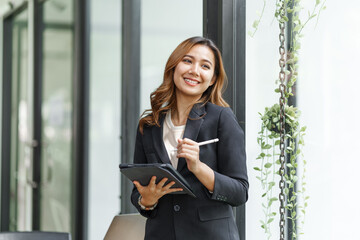 Happy pretty asian businesswoman manager holding touch pad and thinking about something while...