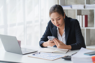 Happy young Asian business woman with a smile using smartphone at the office.