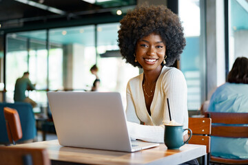 Smiling young african woman sitting with laptop in cafe