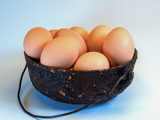 Studio shot of a very battered, burnt and old metalic pot with eggs on a neutral background