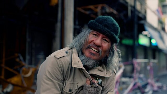 4K, An old, homeless Asian man standing on the side of the road showing a mental disorder like a mad man laughing alone. The problem of homeless people living on the streets