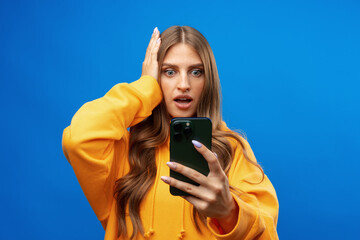 Photo of worried concerned woman looking at her phone against blue background