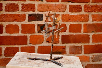 A close up on remnants of an ancient figurine with just its frame made out of wooden crosses remaining and standing on a cloth covered table next to a red brick wall or fence in summer