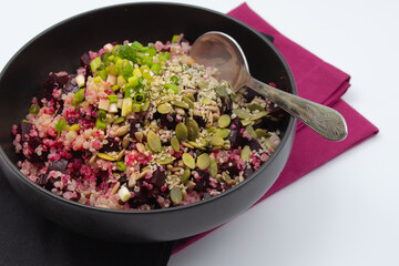 Bowl of quinoa beet salad with seeds and chopped green onions. Dark backround.