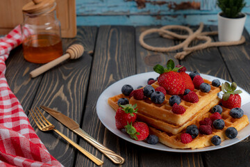 waffles with berries, strawberries and honey on wooden table