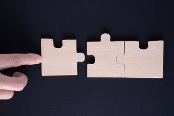 Hand attaches the missing piece of the puzzle. Business concept with wooden jigsaw puzzle on black...