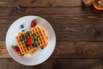 waffles with berries, strawberries and honey on wooden table
