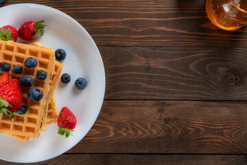 waffles with berries, strawberries and honey on wooden table