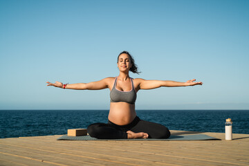 Fototapeta na wymiar Young pregnant woman doing yoga session next the sea - Meditation and maternity concept