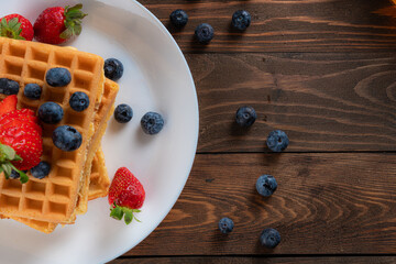 waffles with berries, strawberries and honey on wooden table