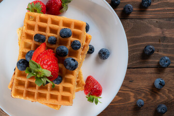 waffles with berries, strawberries and honey on wooden table