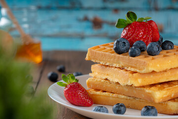 waffles with berries, strawberries and honey on wooden table