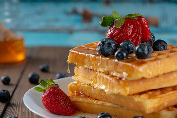waffles with berries, strawberries and honey on wooden table