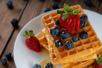 waffles with berries, strawberries and honey on wooden table