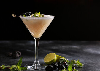 Drinks and cocktails. A light yellow drink with lime, blackberry, mint and ice in a glass on a black table. Bar menu. Background image, copy space