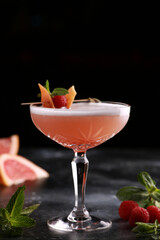 Drinks and cocktails. A light red drink with grapefruit, raspberries, mint and ice in a glass on a black table. Bar menu. Background image, copy space