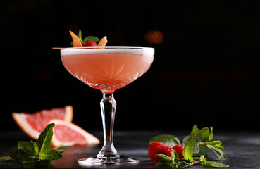 Drinks and cocktails. A light red drink with grapefruit, raspberries, mint and ice in a glass on a black table. Bar menu. Background image, copy space