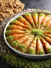 Oriental sweets. Pahlava with nuts, pistachio in a large dish on a black table. Turkish dessert. Background image, copy space, horizontal, top view, flatlay