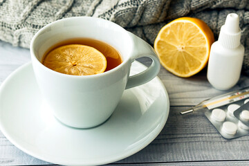 white cup with lemon tea on the background of a thermometer and pills in a blister. The concept of virus prevention and treatment.