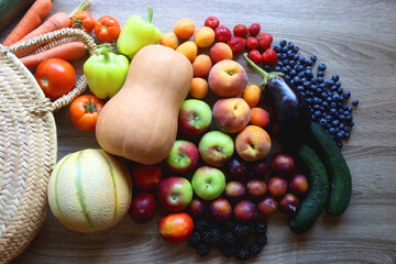 Round straw bag and various healthy fruits and vegetables on wooden background.