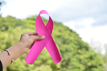 Pink paper ribbon holding in hands of female teenager to show and to call out all people around the world to support and to attend the breast cancer campaign of woman, soft and selective focus.