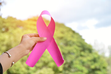 Pink paper ribbon holding in hands of female teenager to show and to call out all people around the world to support and to attend the breast cancer campaign of woman, soft and selective focus.