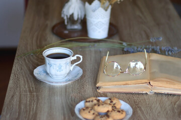 Cup of tea, plate with chocolate chip cookies, open book, reading glasses, lit candles and dry lavender flowers. Hygge at home, selective focus.