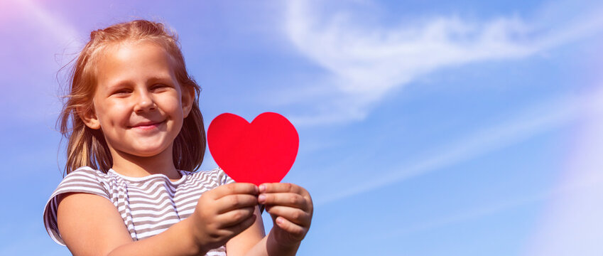 A child with a paper heart in his hands. Congratulations on Valentine's Day. Child on the background of the sky. The concept of lightness and freedom. Happy childhood. Copy space. Banner