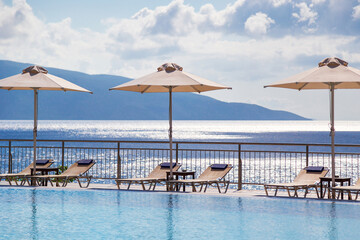 Luxury swimming pool with empty deck chairs and umbrellas at the resort with beautiful sea view