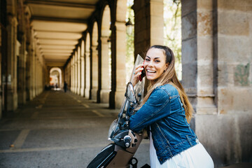Fototapeta premium Young smiling woman on a motorbike talking on a red smartphone