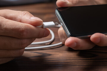Charging a smartphone via a USB cable and a power supply. A black smartphone hanging with a usb charging cable.