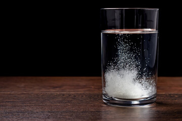 Effervescent tablet in a glass of water close-up on a black background. The concept of health.
