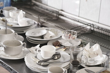 Dirty plates and glasses after a meal in the kitchen in the restaurant. Heap or pile of unclean glass and plates of breakfast or lunch table.