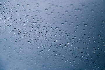 Close up of rain drops on window with blue gray background of dark sky