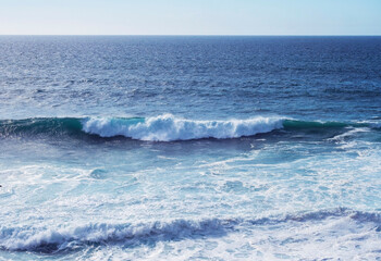 Scenic view of a large blue breaking wave approaching the shoreline of at wild Rota Vicentina coast at Portugal. Atlantic ocean vawes with blue sky at sunny autumn day