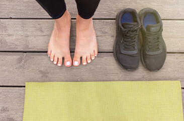 Close-up of bare feet on a wooden floor near a green sports mat, there are black sneakers nearby