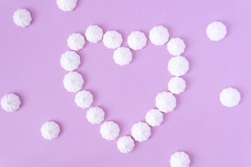 White meringues form a heart shape on a pink background, high angle view.