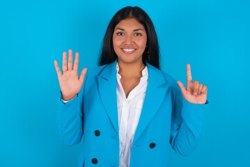 Young latin woman wearing  blue blazer blue background showing and pointing up with fingers number...