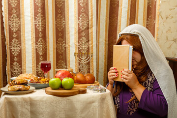 A Jewish woman in a veil falling from her hair prays at the festive table on Rosh Hashanah with a...