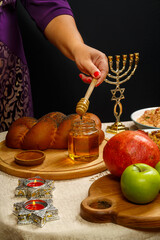 Honey drips from a wooden spoon in a woman's hand next to the menorah challah and couscous and pomegranate.