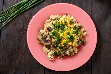 Pasta in a creamy sauce with mushrooms in a plate on the table next to green onion feathers.