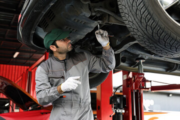 Car mechanic examining car suspension of lifted automobile at repair service station. 