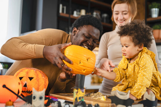 Multi-Ethnic family with the small child preparing for Halloween holiday having fun with jack -o -lantern