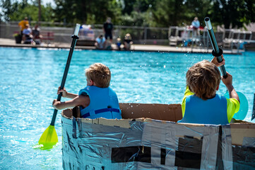 Two boys paddling a cardboard boat in a race in a pool