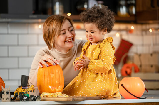Mother and cute little daughter having fun with jack -o -lantern in the kitchen. Halloween holiday