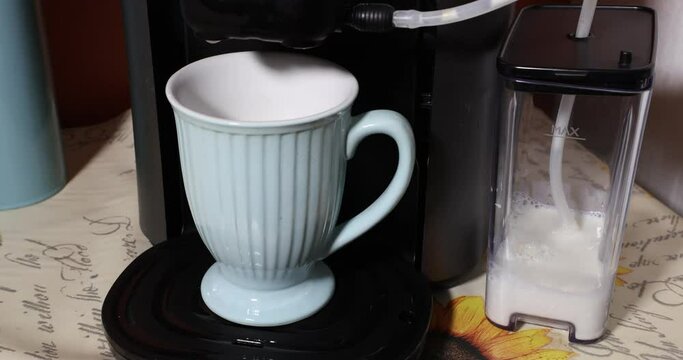 Close-up of coffee being poured into a mug with milk that is in an electric coffee machine to make a delicious latte macchiato, container of frothed milk. Concept of delicious homemade drink