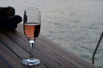 A glass of champagne is on the ship's wooden deck. Evening walk across the lake.