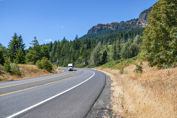 Fototapeta premium Professional white big rig semi truck tractor with semi trailer running for delivery on the turning highway road in scenic nature wild Columbia Gorge area