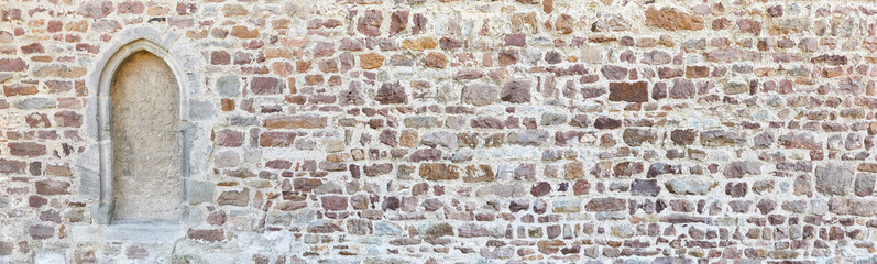 Rustic quarry stone wall with bricked up window, in panoramic format.