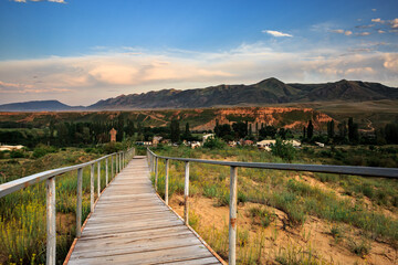 Fototapeta premium Wooden long road at sunset against the backdrop of mountains and a green landscape.
